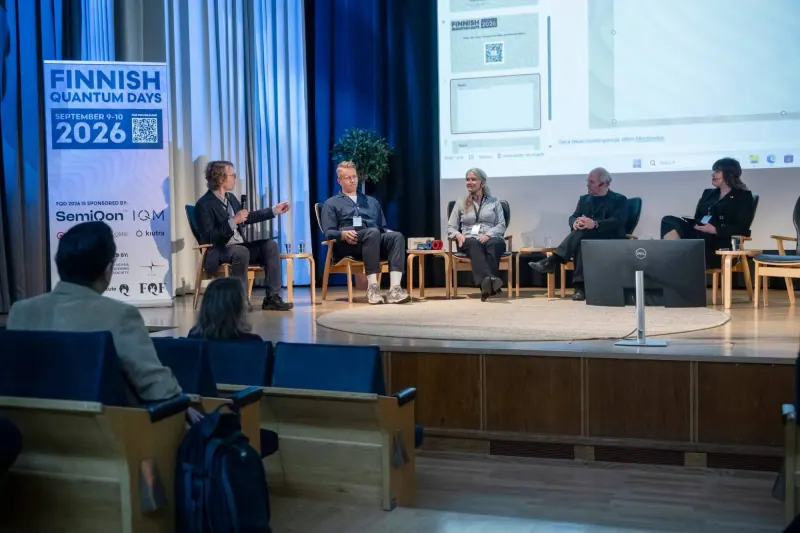 Diskusijos dalyviai sėdi ant scenos pusračiu, moderatorius su mikrofonu kreipiasi į kalbėtojus