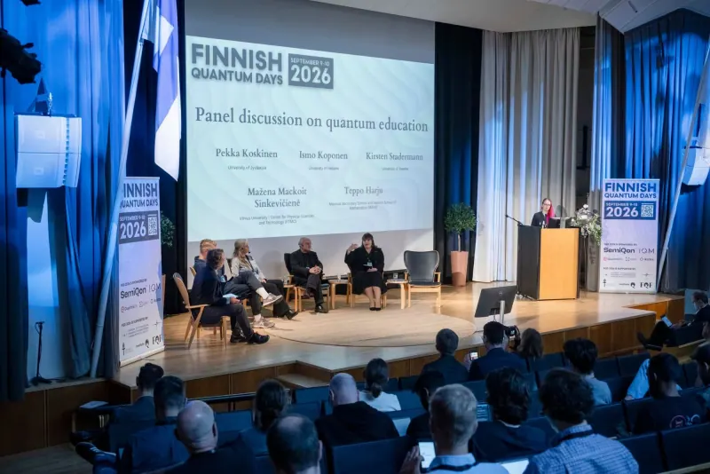 Konferencijos scena: ekrane užrašas „Panel discussion on quantum education“ su dalyvių pavardėmis, ant scenos sėdi diskusijos dalyviai, salėje – žiūrovai