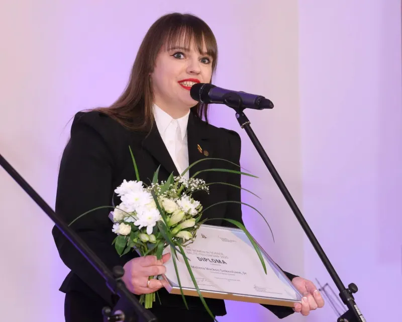 Me speaking into a microphone, holding the diploma and flowers